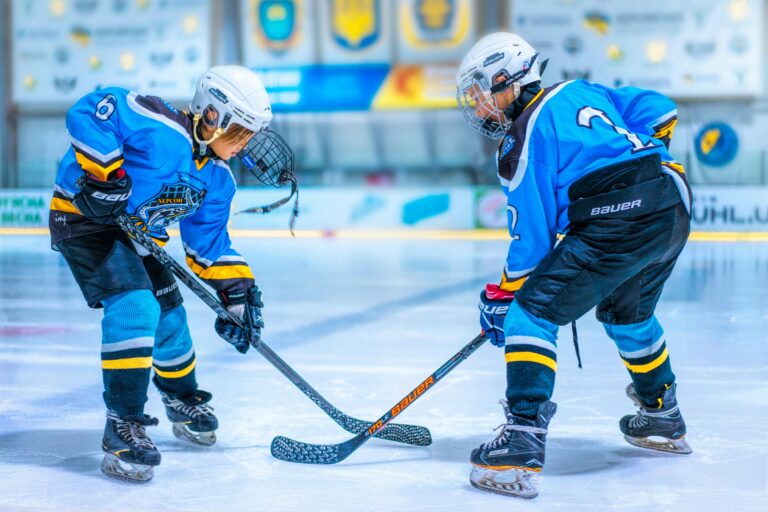 Two young athletes face-off during an ice hockey game in an indoor rink.