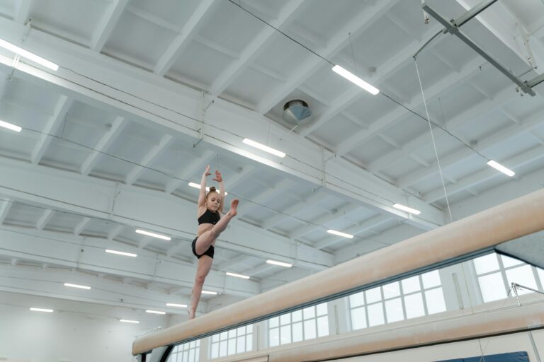 A young gymnast gracefully executing a routine on the balance beam in an indoor gym.