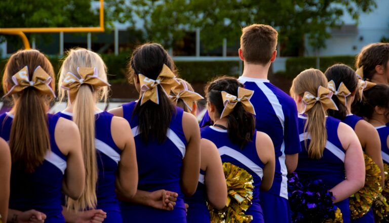 Rear view of cheerleaders in uniform outdoors, preparing for performance.